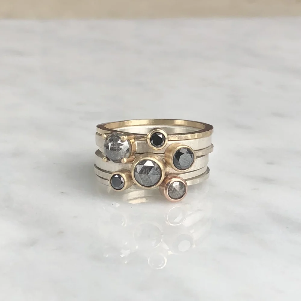 Stacked rings with black and gray gemstones on a white marble surface.