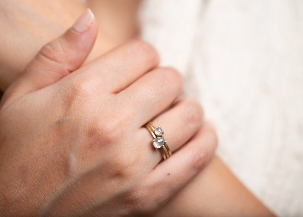 A close-up of a person's hand wearing multiple gold rings with diamonds, resting on their chest.