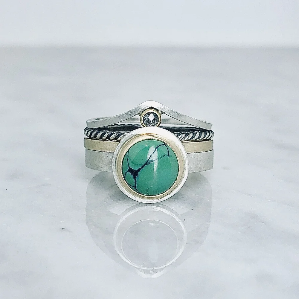 Stack of rings including a turquoise stone ring, a thin band with a small diamond, a twisted rope band, and plain bands, all silver or silver-toned.