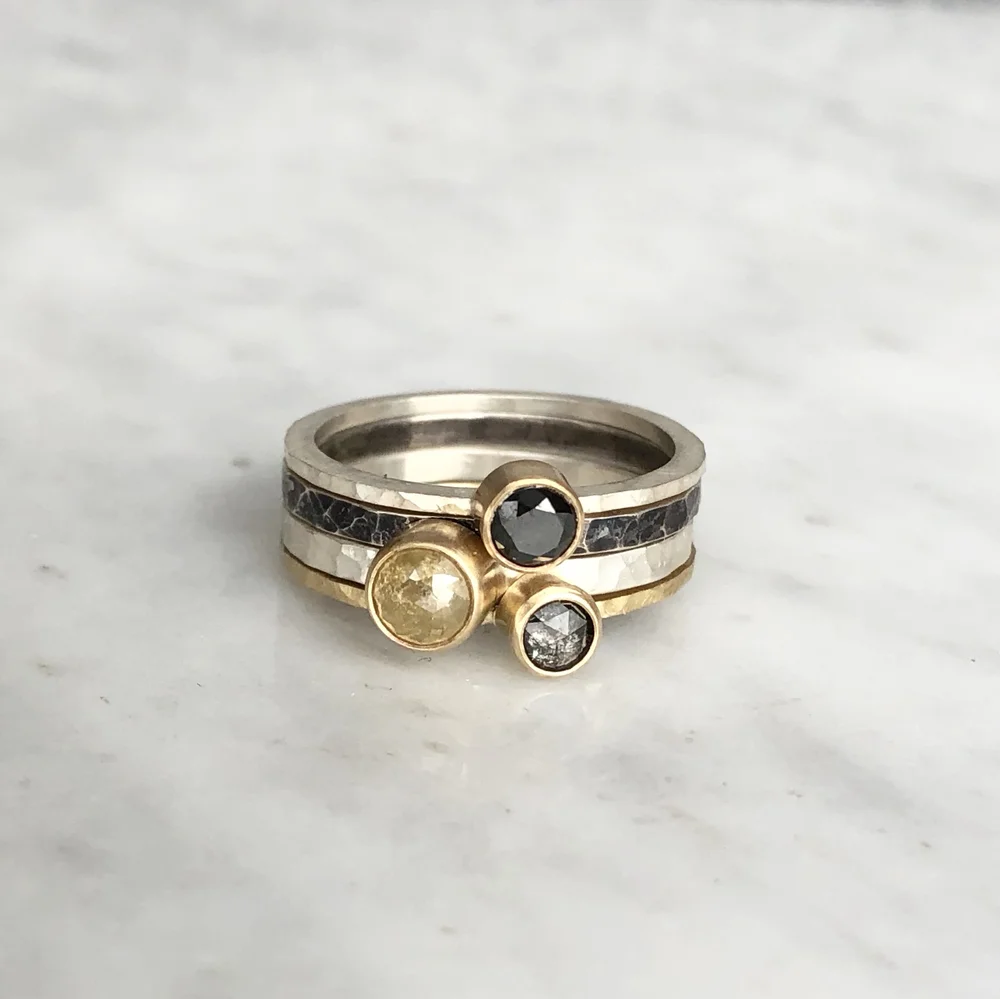 Three stacked rings with black, yellow, and gray gemstones on a white marble surface.