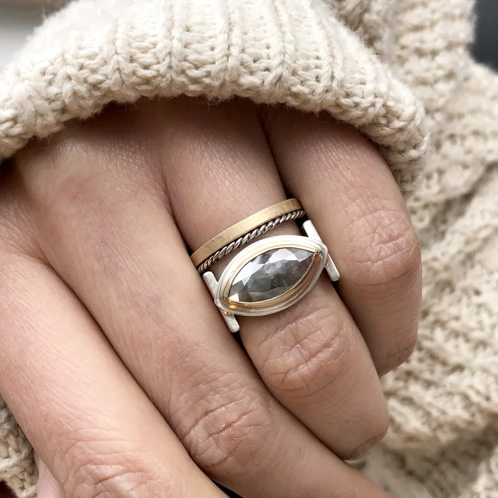 Close-up of a hand wearing three rings on the middle finger, with a textured beige knit fabric sleeve nearby.