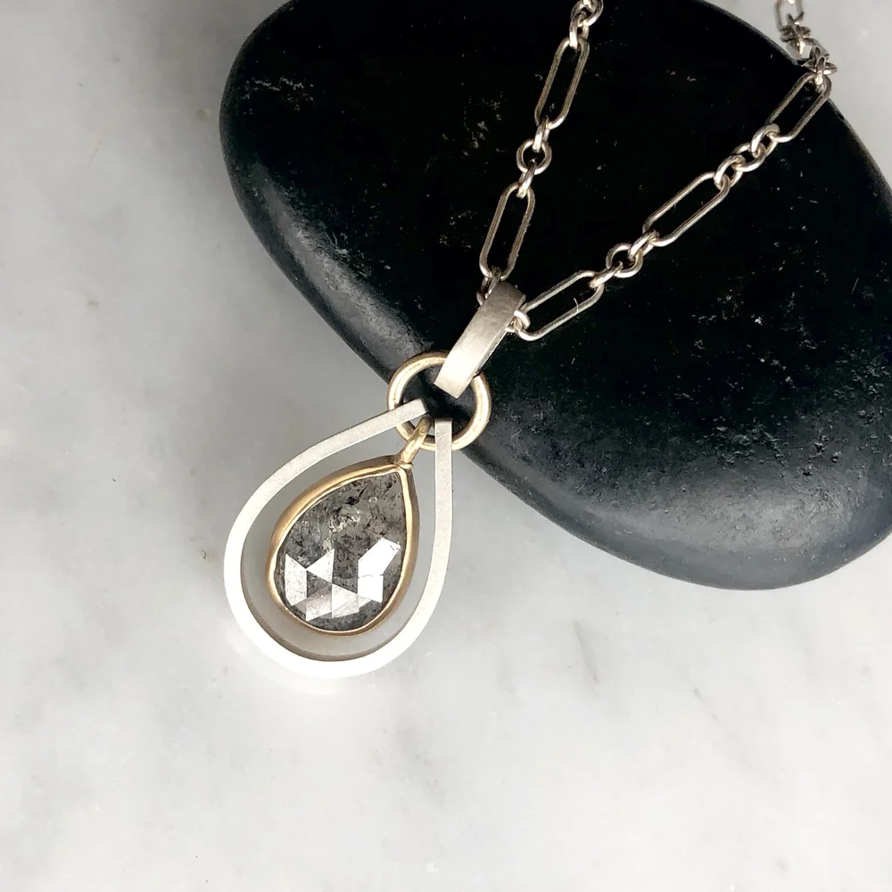 A necklace with a teardrop-shaped pendant featuring a faceted black gemstone, resting on a black stone surface against a white background.