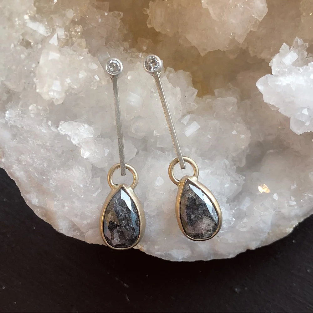 Sterling silver and 14 K yellow gold earrings with pear-shaped salt and pepper diamonds, placed on a crystalline white surface.