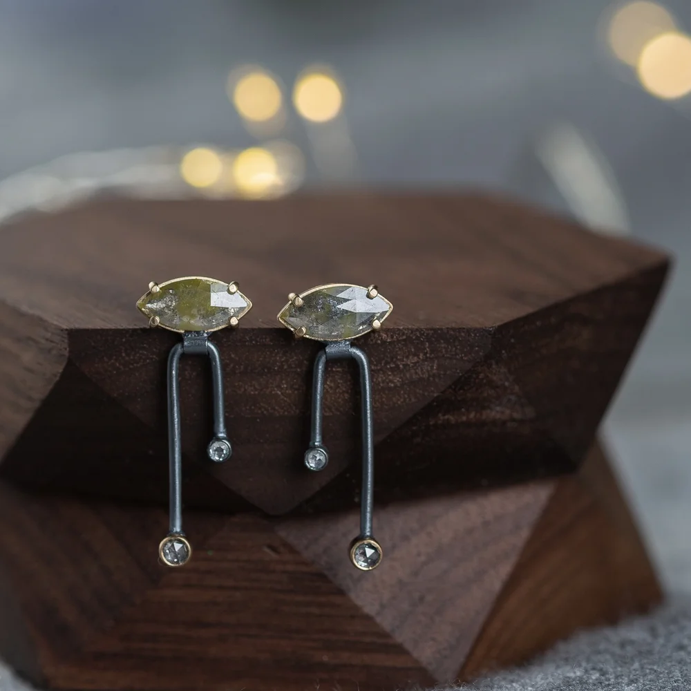 Elegant earrings with marquise-shaped yellow stones and small round diamonds, displayed on a dark wooden stand.