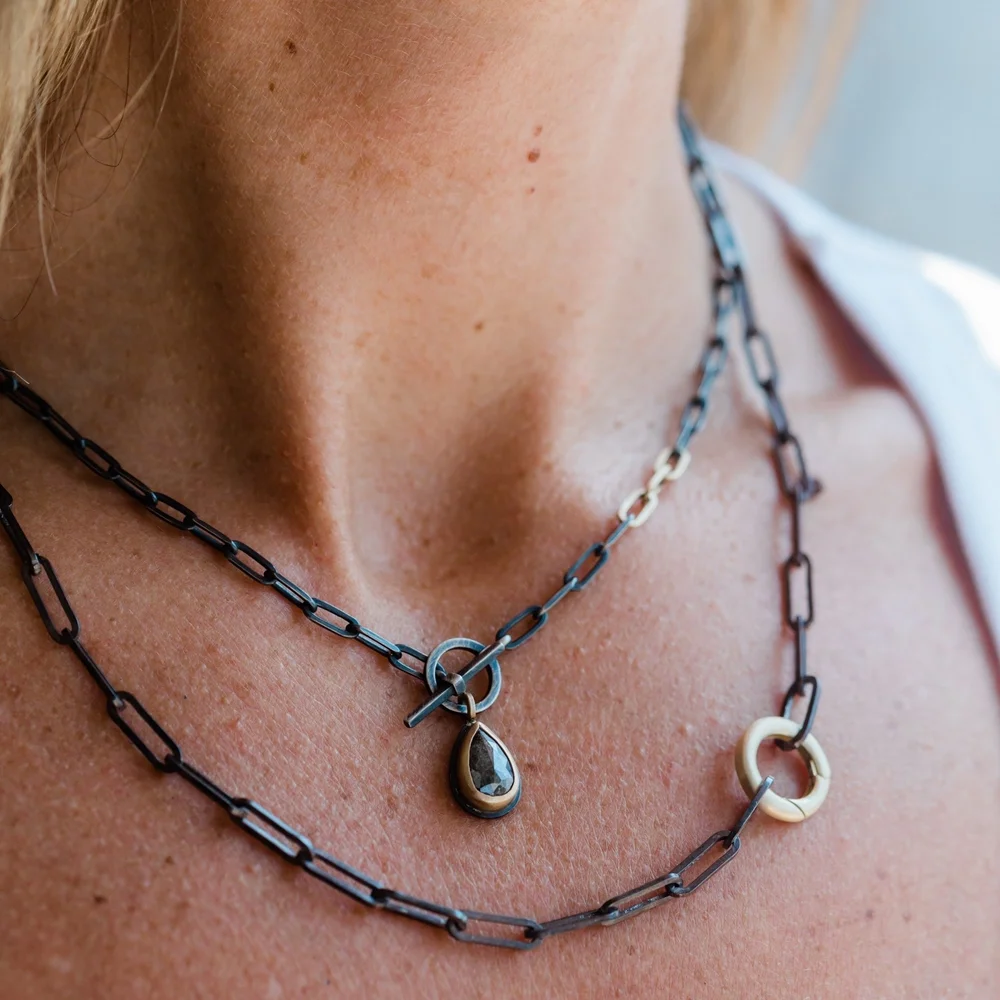 Close-up of a woman's neck showing two layered necklaces with different chain links and pendant charms.