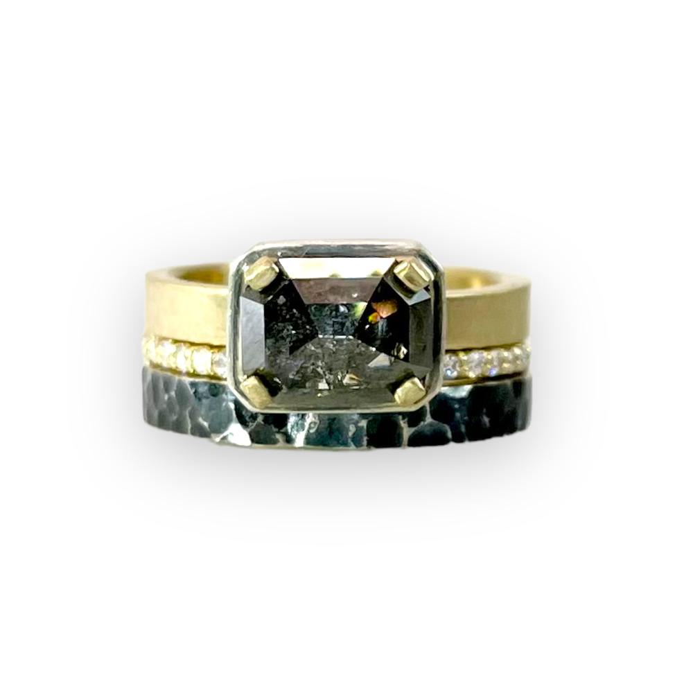 Close-up of a ring with a black gemstone in a square setting, accented by small diamonds on the band.